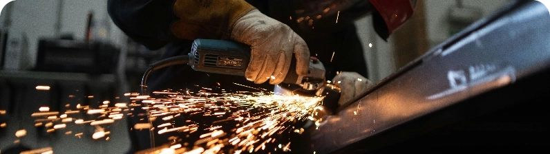 Close-up of a worker grinding metal with a handheld angle grinder, sparks flying.