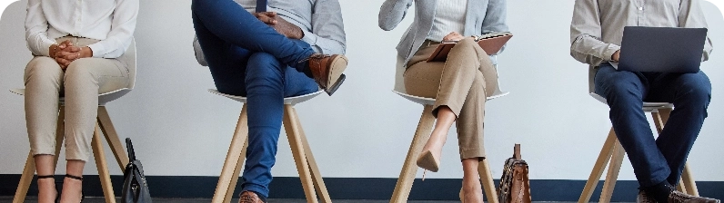 Four people seated in a row on chairs, each with a notebook or laptop, suggesting a panel discussion or meeting.
